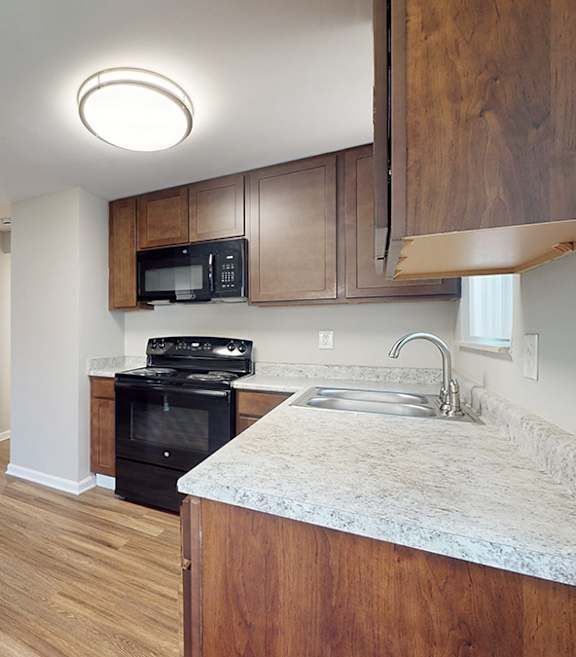 A black refrigerator stands in a kitchen with white cabinets and a black countertop.