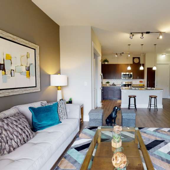A living room at Lofts at Watters Creek with a couch, TV, and coffee table, and a kitchen in the background. 