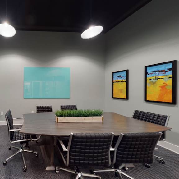 The conference room with a large conference table surrounded by chairs, artwork on the walls, and a TV at Loft at Watters Creek.  