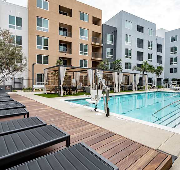 A pool surrounded by lounge chairs and umbrellas in front of apartment buildings. at Baker Block, California