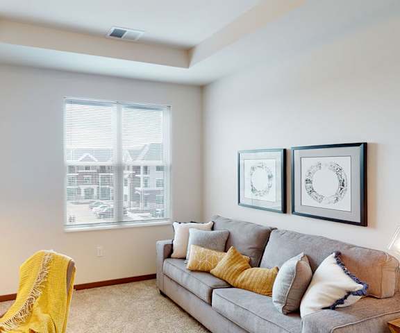 A modern office with a desk, chair, couch with pillows, windows, shelves, coffee table, wall art, decorations, and large window with light streaming in at Van Buren West Apartment Homes. 