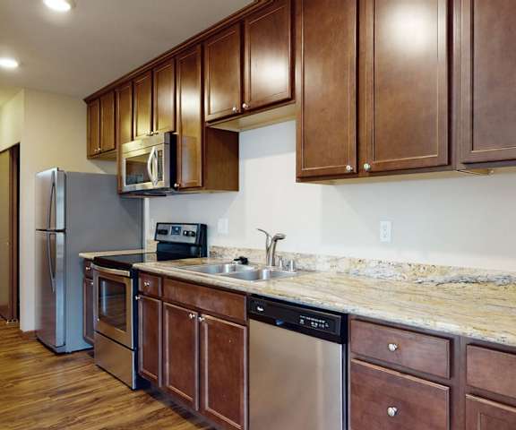 A large kitchen with stainless steel appliances, spacious marble countertops, and large wooden cabinets at Ondine at Juanita Bay Apartments. 