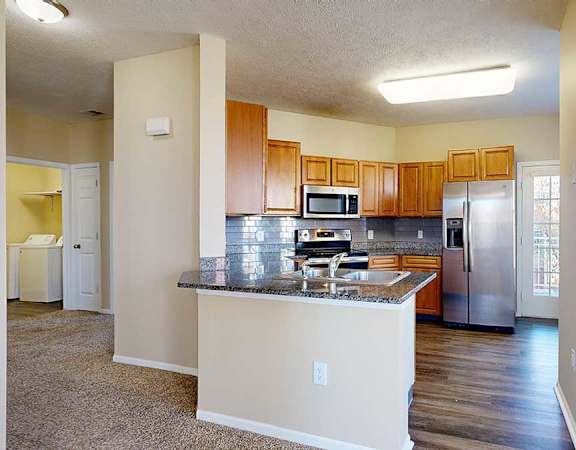 a kitchen featuring wooden cabinets, granite countertops, a peninsula, a tile backsplash, hardwood floors, and stainless steel appliances
