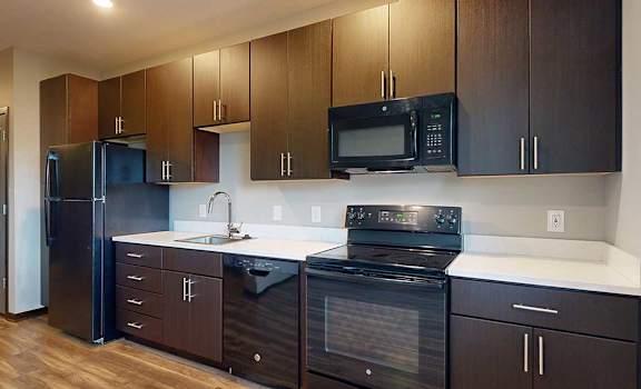 a kitchen with dark wood cabinets, white granite countertops, and black appliances