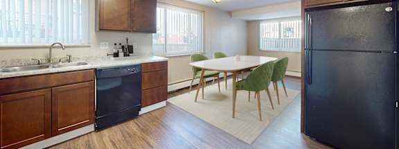 A kitchen with a black fridge and a dining table with chairs.