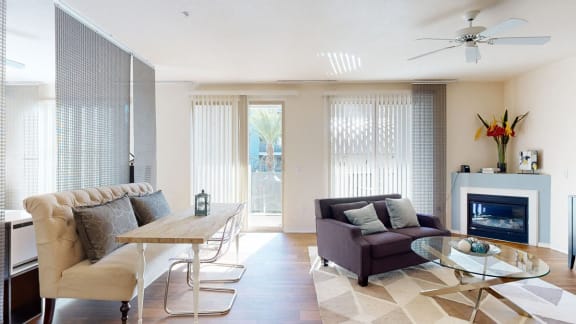 The spacious living room with a couch, plush chairs, coffee table, overhead lighting with a ceiling fan, decorations, a TV, and a table and chairs at Rio Paradiso Apartment Homes. 