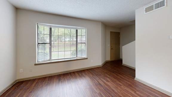 A room with wooden floors and a window with blinds.