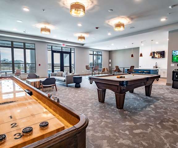 A wonderful resident lounge with tables, chairs, a pool table, a shuffleboard table, TVs, arcade games, couches, plush chairs, and a kitchen with overhead lighting at Van Buren East Apartment Homes.  at