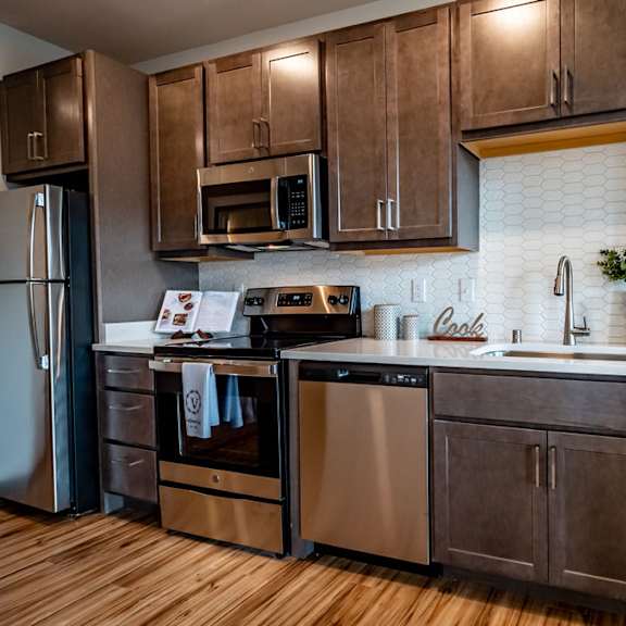 A kitchen with stainless steel appliances and dark wooden cabinets at Van Buren East.