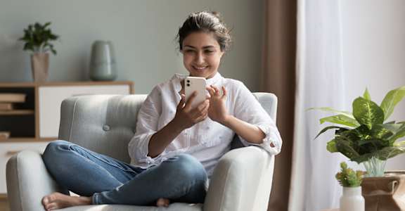 A woman is sitting on a chair and holding a phone.