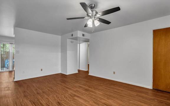 an empty living room with wood floors and a ceiling fan