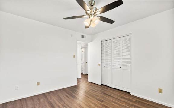 an empty living room with a ceiling fan and a closet