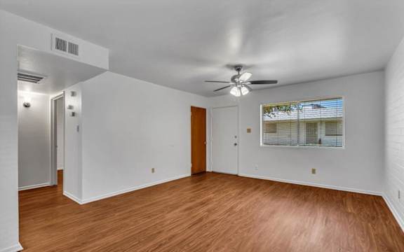 an empty living room with wood floors and a ceiling fan