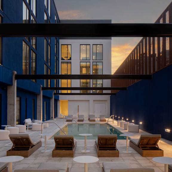 A modern outdoor pool area with lounge chairs and tables at Miles at Ybor Apartments, Florida