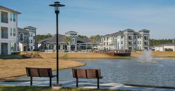 Two benches are in the foreground of a park with a lake and a building in the background.