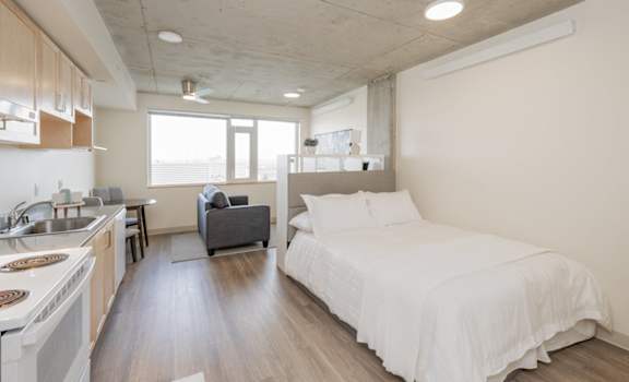 A modern bedroom with a large bed and a kitchen area.