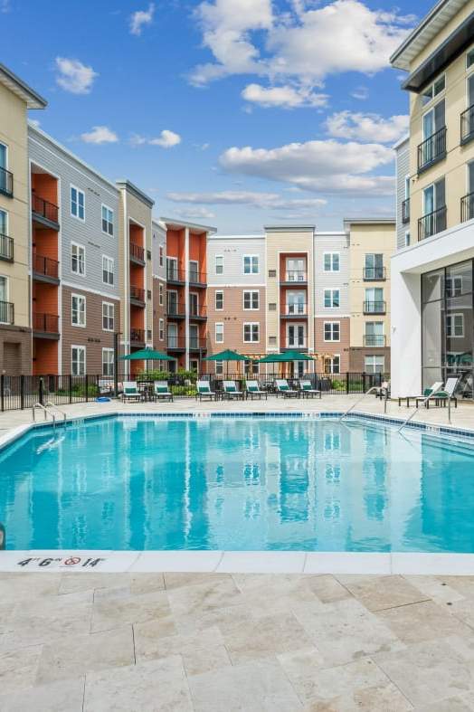 an outdoor swimming pool with lounge chairs in front of an apartment building