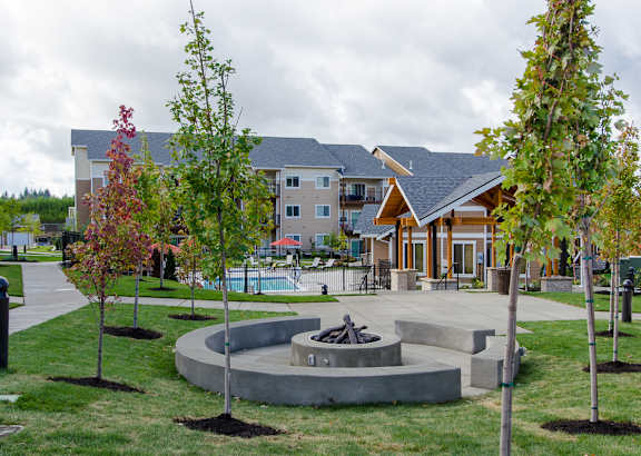 a fire pit in the middle of a grassy area with a building in the background