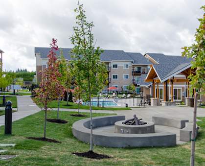 a fire pit in the middle of a grassy area with a building in the background