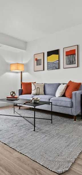 A living room with a grey sofa and a glass table at Park On Canal Apartments - Clinton Twp, MI Apartments, Michigan