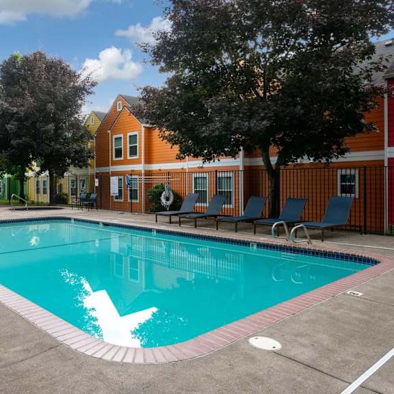 A swimming pool surrounded by chairs and trees.