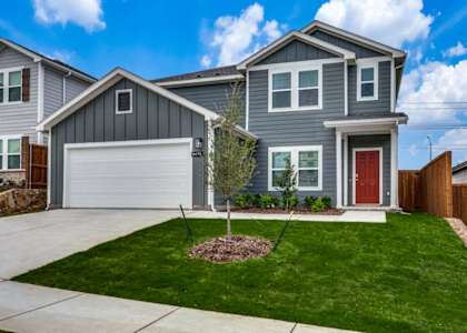 A grey house with a red door and a small tree in the front yard.