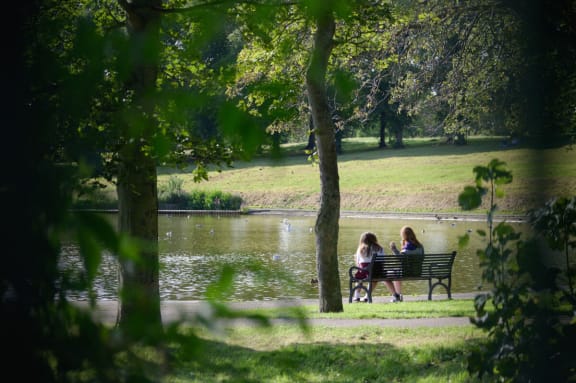 two women sitting on a park bench next to a lake