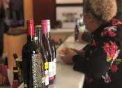 Thumbnail 4 of 9 - a woman sits at a counter with four bottles of wine