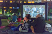 Thumbnail 7 of 9 - a couple sitting on a blanket watching a movie in a park at night