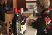 Thumbnail 4 of 9 - a woman sits at a counter with four bottles of wine
