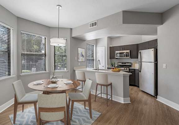 A kitchen with a table and chairs in the foreground and a refrigerator in the background.