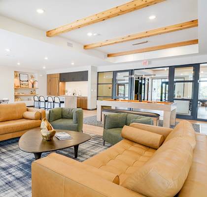 an apartment clubroom with tan leather couches, a kitchen, and a pool table