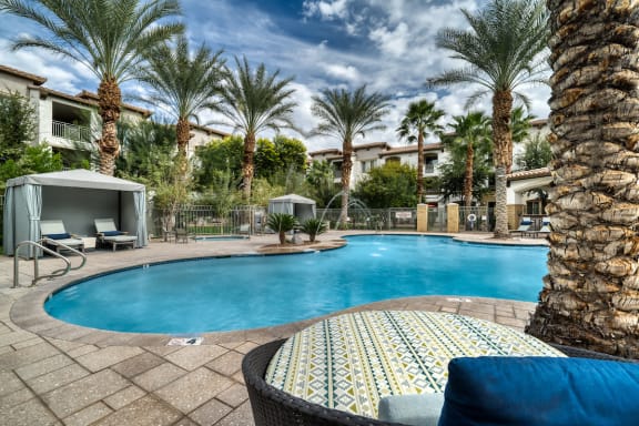 A pool surrounded by palm trees and a patio area with a couch and umbrella at Monument, Chandler, AZ 85224