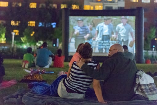 a couple sitting on a blanket watching a movie in a park at night