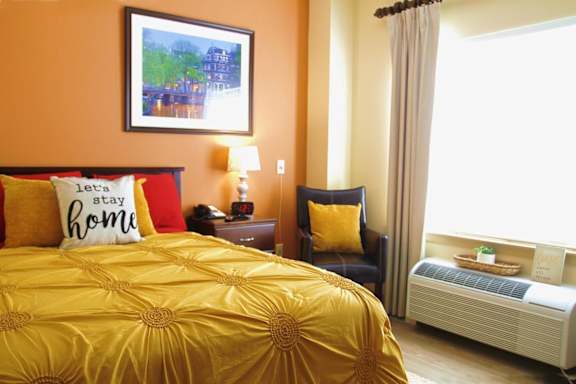 A bedroom with a bed, nightstand, chair, and window.