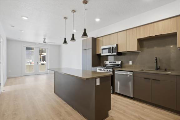 A modern kitchen with a dark brown island and stainless steel appliances at Brickside Heights, Millcreek, UT, 84106