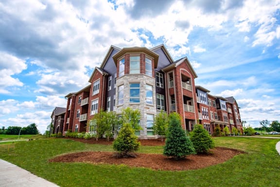 an apartment building with green grass and a cloudy sky