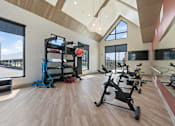 Thumbnail 19 of 52 - A gym with a row of exercise bikes and a weight rack at Solhavn Apartments, American Fork