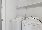 Thumbnail 23 of 25 - Two white front loading washing machines in a small laundry room.
