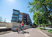 Thumbnail 7 of 8 - a woman riding a bike in front of a building at CityWay Apartments, Indianapolis, IN, 46204