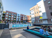 Thumbnail 1 of 8 - people sitting on benches in front of an apartment complex at CityWay Apartments, Indianapolis, IN, 46204