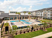 Thumbnail 4 of 25 - Aerial view of a luxury community pool featuring in-water lounge seating, beautifully landscaped grounds, and modern amenities.