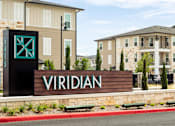 Thumbnail 9 of 25 - Modern apartment community entrance sign surrounded by landscaped grounds and upscale residential buildings.