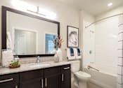 Thumbnail 17 of 25 - Modern bathroom featuring a spacious vanity, granite-style countertops, and a sleek tub-shower combination.