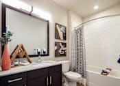 Thumbnail 18 of 25 - Modern bathroom featuring a spacious vanity, granite-style countertops, and a sleek tub-shower combination.