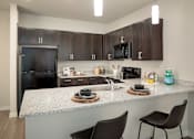 Thumbnail 11 of 25 - Modern kitchen featuring dark cabinetry, granite-style countertops, and convenient bar seating for casual dining.