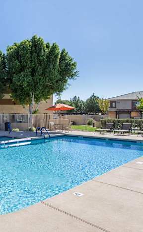 A large swimming pool surrounded by trees and a building in the background at Sereno Townhomes, Arizona.