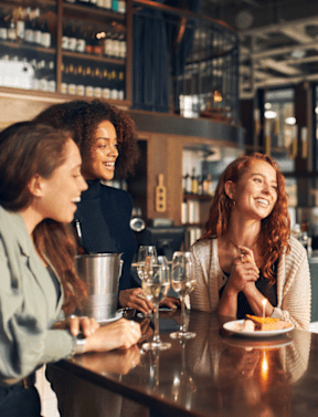 A group of people are gathered around a bar counter, enjoying drinks and conversation.at Foothills Court Apartments, Phoenix, 85029