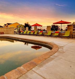 A pool surrounded by chairs and umbrellas with a sunset in the background.