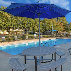 A blue umbrella is next to a table and chairs by a pool.